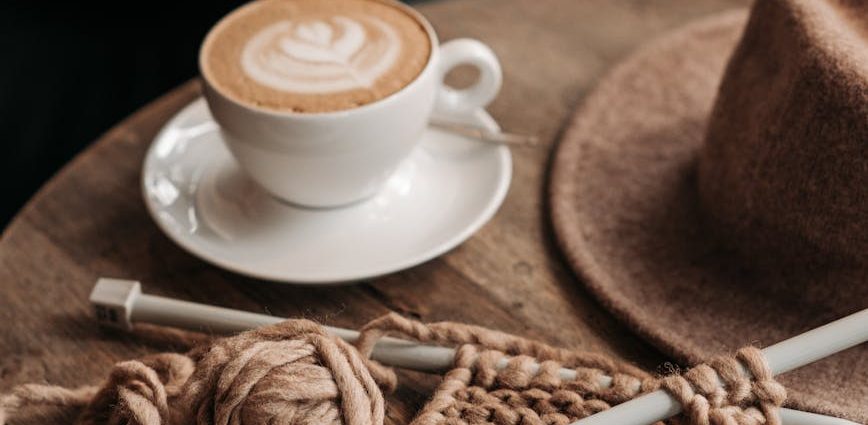 coffee drink beside a knitted material on wooden table